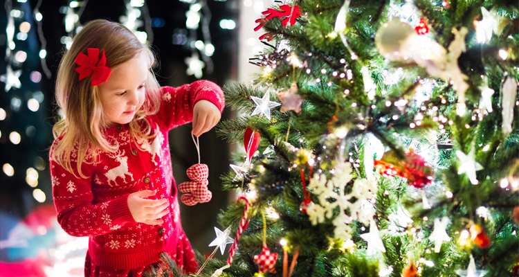 little girl hanging an ornament on Christmas tree
