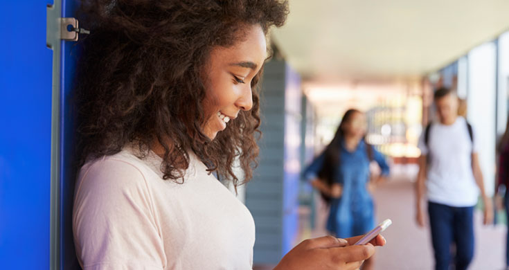 female student texting in school hallway