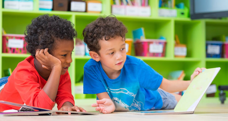 Two boys lay down on floor and reading book in preschool library