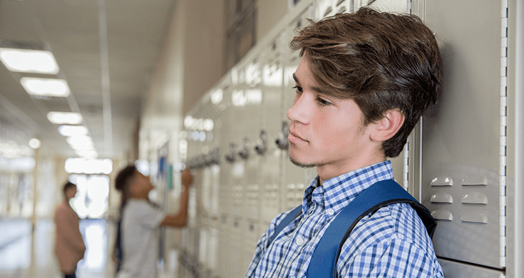 high school student leaning against locker with sad expression