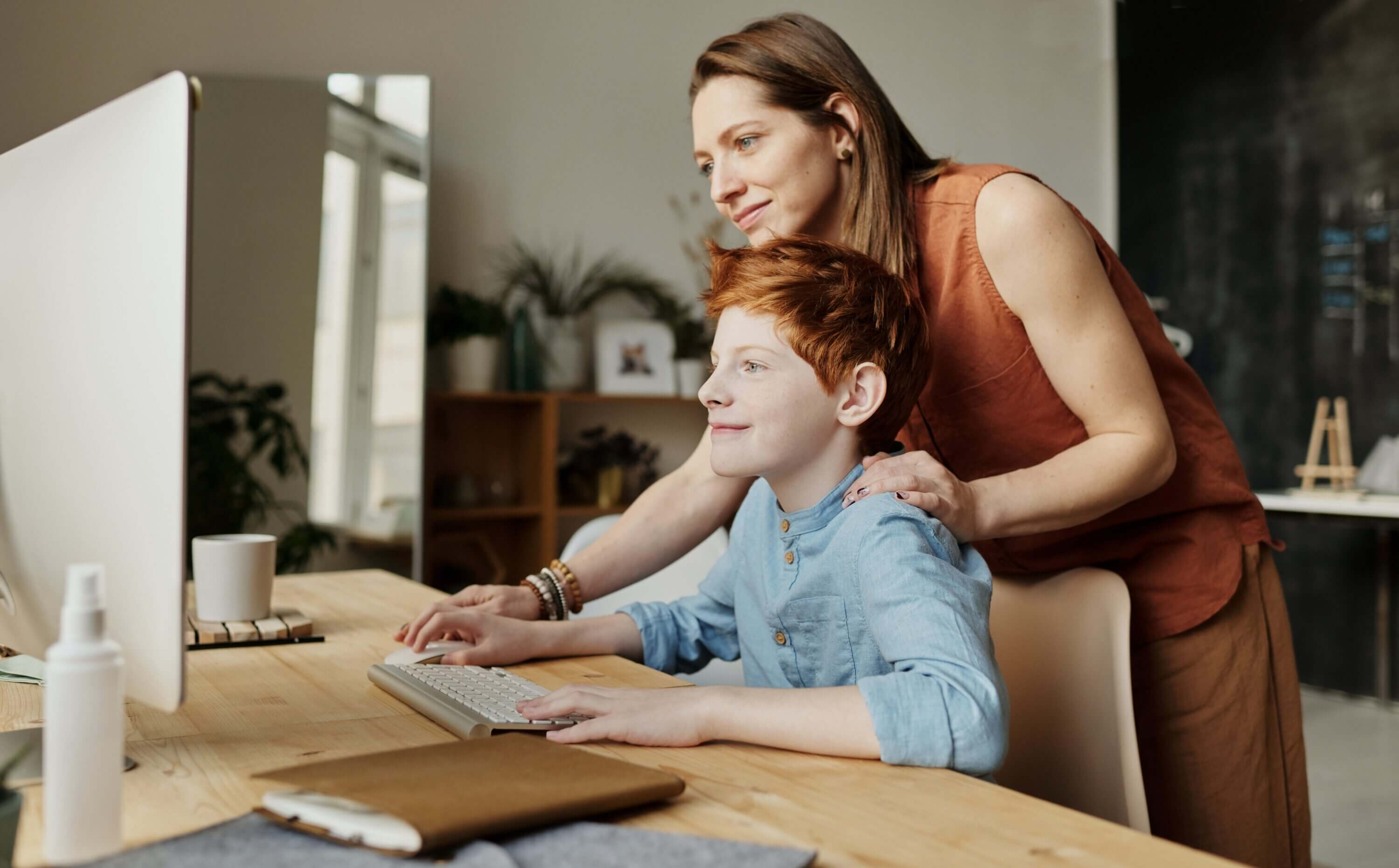 A parent helps their child with their online school.