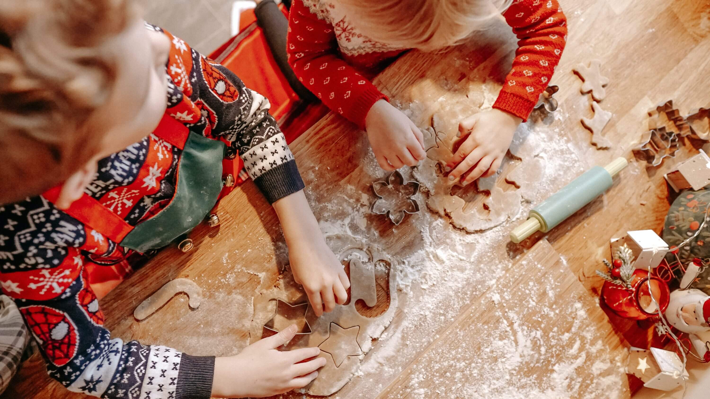 Two children use cookie cutters and a rolling pin to make holiday cookie cutouts.