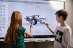 Two students build a vehicle on an interactive white board