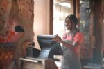 A teen smiles as she inputs an order in a POS within a cafe.