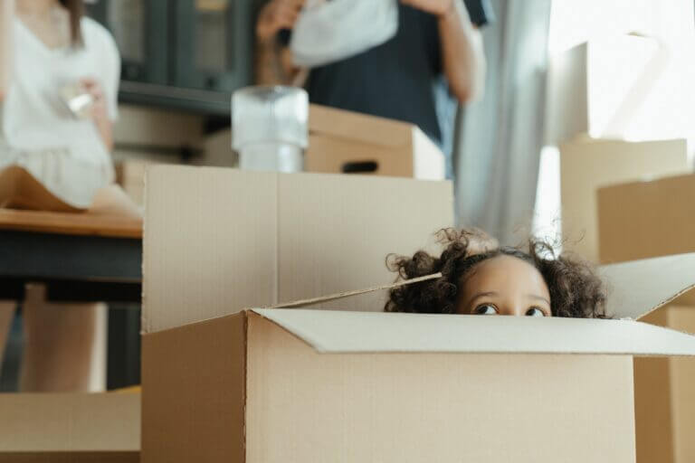 A girl plays in a moving box while her parents unpack in their new home.