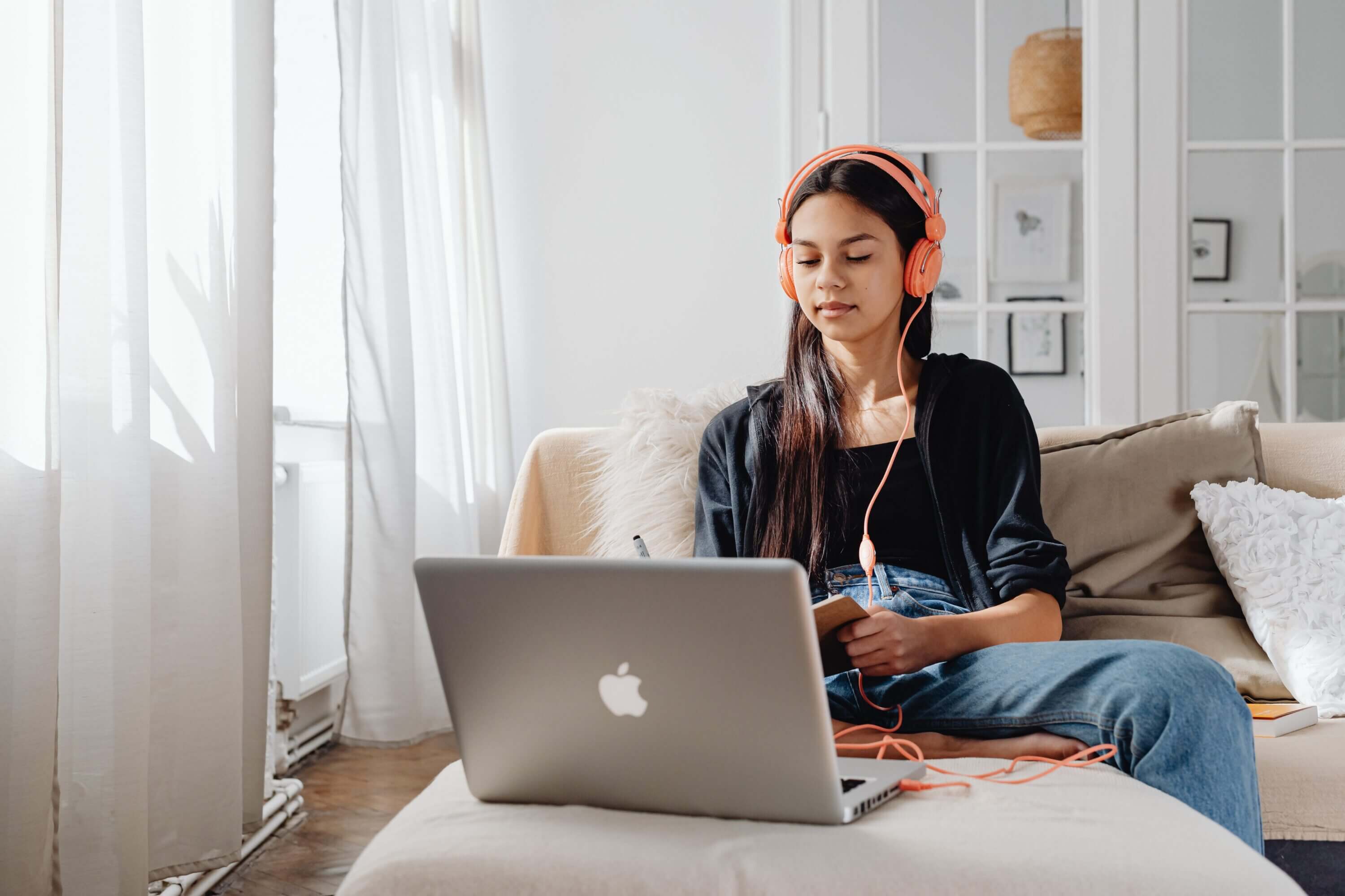 A girl wears headphones while she works at her laptop on her online school.