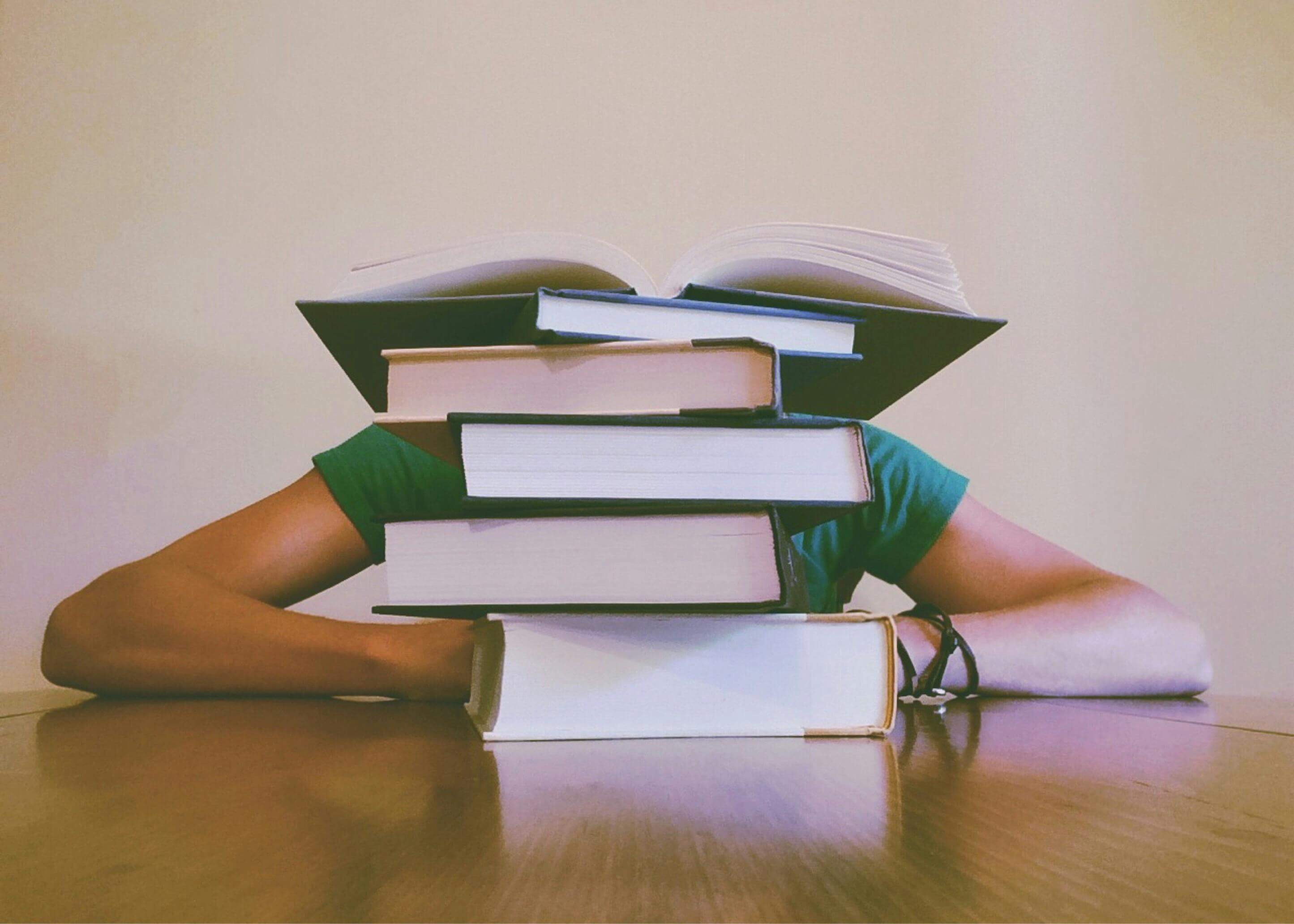 A student rests behind a pile of books.
