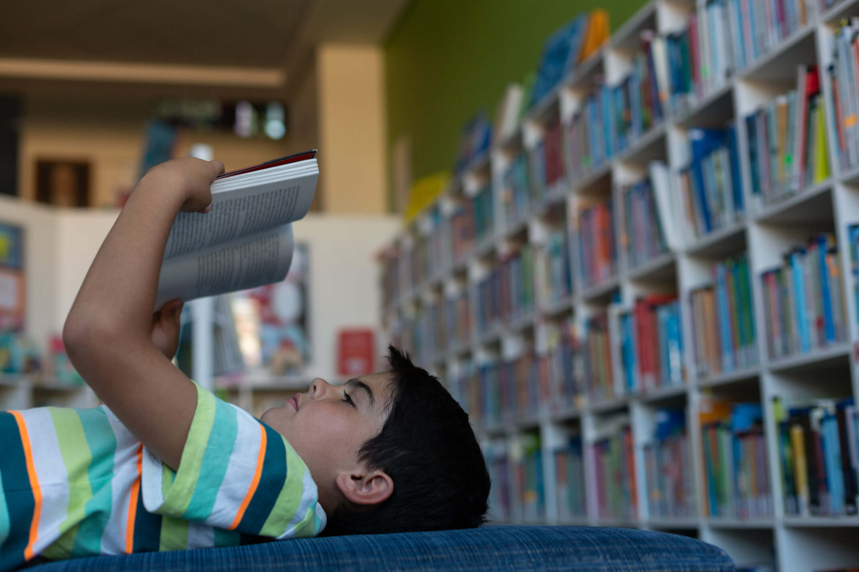 A boy lays down to read a book in a library