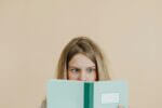 A girl reads a poem in a green book with a slightly confused look on her face.