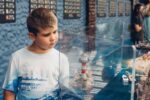 a young boy looks at a glass case display featuring a lighthouse