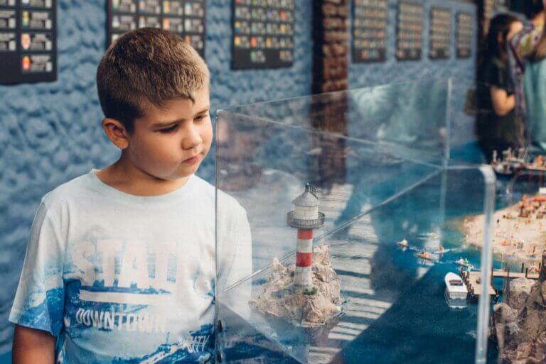 a young boy looks at a glass case display featuring a lighthouse